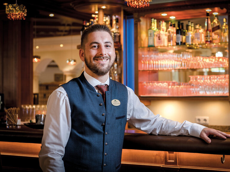 Ein Hotel Mitarbeiter für den Service steht vor der gut ausgestatteten Bar im Wellness & SPA Resort Mooshof in Bayern.
