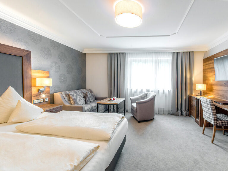 Das Zimmer Typ 5 im Hotel Mooshof in Bayern bietet modernes Design mit einem komfortablen Bett und einem Flachbildfernseher über einen Holzschreibtisch.