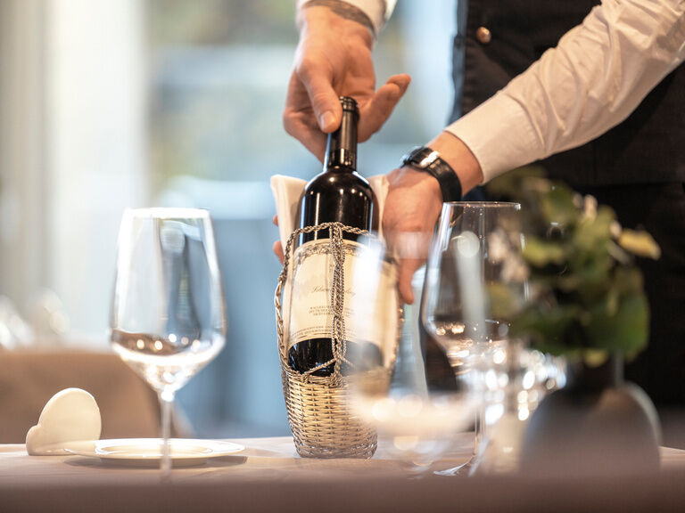 Ein Serviceteam Mitarbeiter präsentiert eine edle Flasche Wein vom Hotel Mooshof im Bayerischen Wald, umgeben von elegantem Tischgedeck.