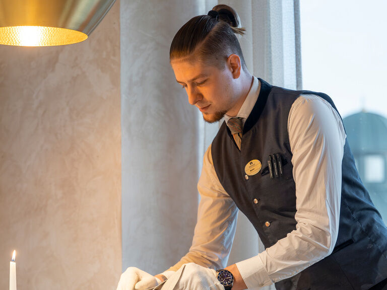 Ein Serviceteam Mitarbeiter des Wellnesshotels Mooshof im Bayerischen Wald deckt einen Tisch im Restaurant für die Gäste ein.