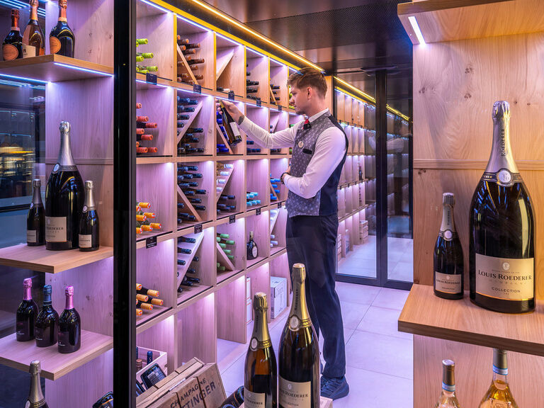 Ein Mitarbeiter sucht im Weinklimaraum des Wellnesshotels Mooshof eine hochwertige Flasche Wein für einen Kunden aus.